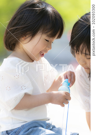 Little sisters playing in the fresh green early summer park 102093300
