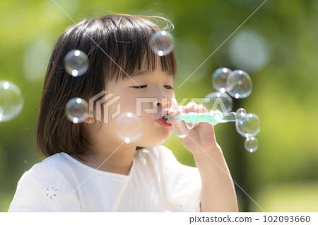 A little girl playing with soap bubbles in a fresh green early summer park A little girl playing with soap bubbles in a fresh green early summer park 102093660