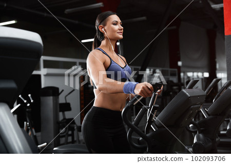 Young woman working out on elliptical trainer in modern gym Young woman working out on elliptical trainer in modern gym 102093706