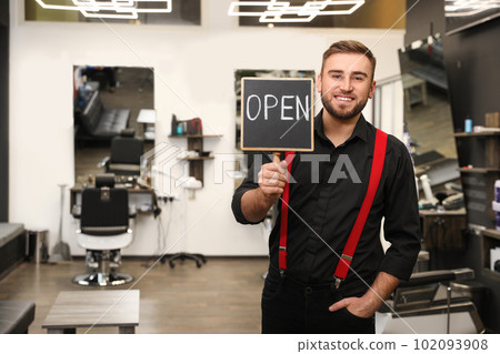 Young business owner holding OPEN sign in his barber shop 102093908