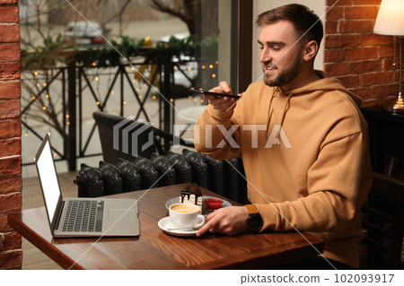 Male blogger taking photo of dessert and coffee at table in cafe 102093917