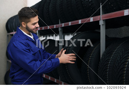 Male mechanic with car tire in auto store 102093924