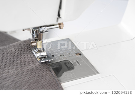 Modern sewing machine presser foot with gray fabric and thread, closeup Modern sewing machine presser foot with gray fabric and thread, closeup 102094158