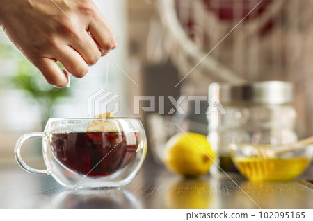 Woman puts the tea bag in the glass cup with hot water Woman puts the tea bag in the glass cup with hot water 102095165