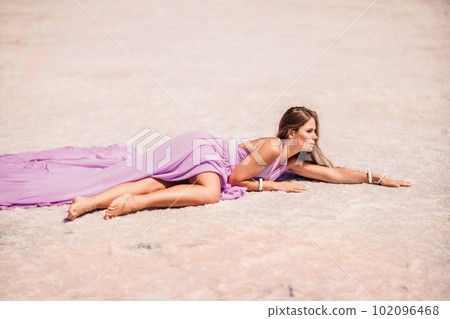 A woman in a pink dress lies on the shore of a pink lake, takes a photo for memory and leaves unforgettable memories. A woman in a pink dress lies on the shore of a pink lake, takes a photo for memory and leaves unforgettable memories. 102096468