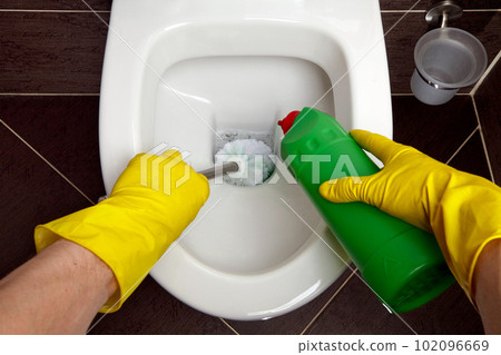 A single man in yellow rubber gloves cleans the toilet bowl with a brush and disinfectant 102096669