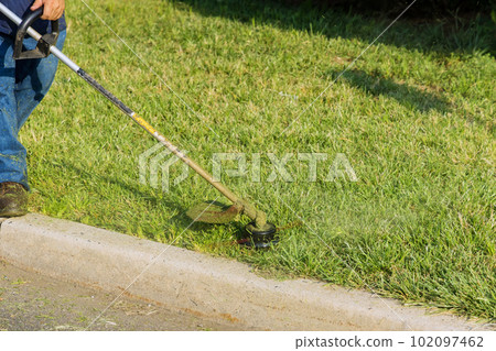 Municipal worker with lawn mower mows fresh green grass near road using hand lawn mower 102097462