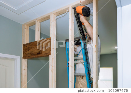 An air hammer is being used by builder to nail wooden beams to housing frameworks so that they can be constructed An air hammer is being used by builder to nail wooden beams to housing frameworks so that they can be constructed 102097476