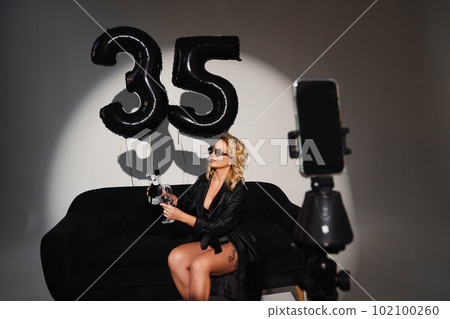 a blonde in a black with champagne on the couch. balloons of numbers thirty-five 102100260