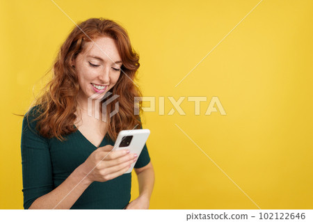 Happy redheaded woman smiling while using the mobile 102122646