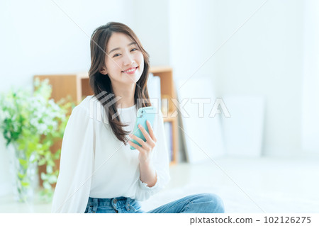 一個年輕的女人，在客廳裡操作智能手機 102126275