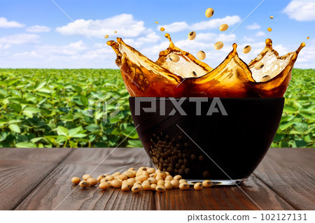 splashing soy sauce in glass bowl on table with green soybean field as background splashing soy sauce in glass bowl on table with green soybean field as background 102127131