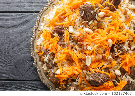Afghan national dish Kabuli Pulao rice pilaf with lamb and raisin, carrot, nut, spices closeup on the plate. Horizontal top view Afghan national dish Kabuli Pulao rice pilaf with lamb and raisin, carrot, nut, spices closeup on the plate. Horizontal top view 102127402