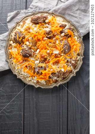 Delicious colorful Afghan rice pilaf Kabuli pulao with lamb and raisin, carrot, nut, spices closeup on the plate. Vertical top view Delicious colorful Afghan rice pilaf Kabuli pulao with lamb and raisin, carrot, nut, spices closeup on the plate. Vertical top view 102127403