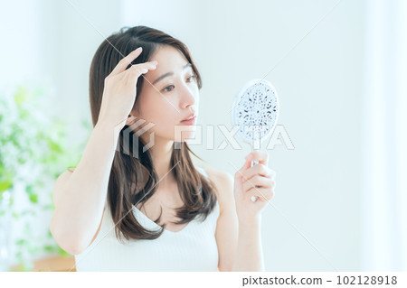 A young woman doing skin care while looking at a hand mirror in the living room A young woman doing skin care while looking at a hand mirror in the living room 102128918