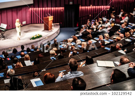 Business and entrepreneurship symposium. Female speaker giving a talk at business meeting. Audience in conference hall. Rear view of unrecognized participant in audience. Business and entrepreneurship symposium. Female speaker giving a talk at business meeting. Audience in conference hall. Rear view of unrecognized participant in audience. 102129542