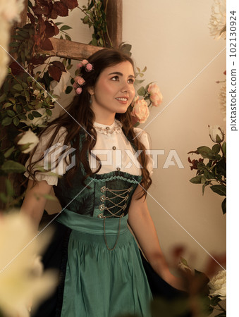 A young peasant woman standing in a garden with flowers dressed in a 19th century bavarian dress. 102130924