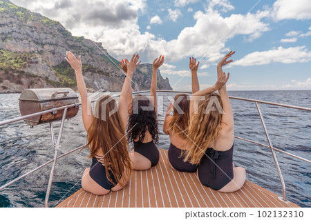 Womans on a yacht. Happy models in a swimsuit posing on a yacht against a blue sky with clouds and mountains Womans on a yacht. Happy models in a swimsuit posing on a yacht against a blue sky with clouds and mountains 102132310