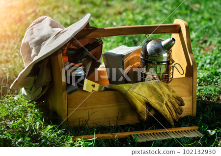 Beekeeping equipment. A tool of the beekeeper. Everything for a beekeeper to work with bees. Smoker, a chisel, a box, beekeeper suit for protection from the bees. Photo on the topic of beekeeping. 102132930