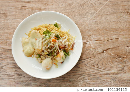 dry Chinese yellow egg noodles topping boiled chop pork and ball on plate 102134115