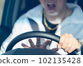 The hand of a middle-aged male driver who holds the steering wheel while shouting and sounds the horn 102135428