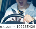 The hand of a middle-aged male driver who holds the steering wheel while shouting and sounds the horn 102135429