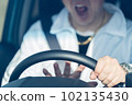 The hand of a middle-aged male driver who holds the steering wheel while shouting and sounds the horn 102135430