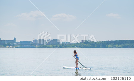 Caucasian woman in a striped swimsuit rides on a SUP board. The girl prefers active rest. 102136110