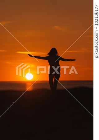 silhouette at sunset, person dancing and rejoicing against background of orange sky and sun 102136177