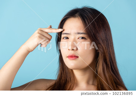 Beauty skin care concept. Asian young woman pointing eyebrow with her finger studio shot isolated on blue background, beautiful portrait female point face and forehead 102136895