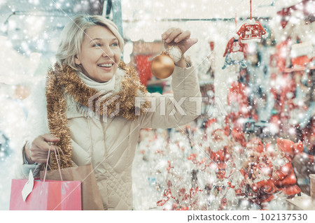 Happy mature woman in tinsel with Christmas toys at fair Happy mature woman in tinsel with Christmas toys at fair 102137530
