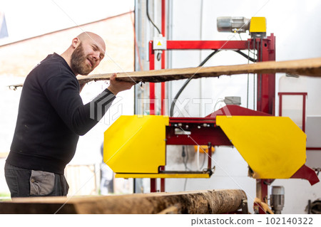 Young handsome joiner man cutting wood board, processing the wood, huge wood cutter or saw, industrial concept 102140322