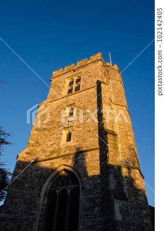 A historic stone block church bathed in the setting sun on the outskirts of London 102142405