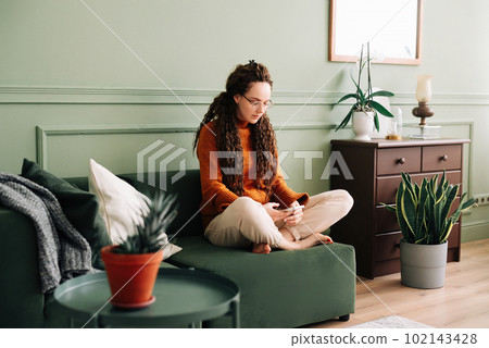 Young woman relaxing and shopping online with smartphone at home. Happy lady enjoying social media 102143428