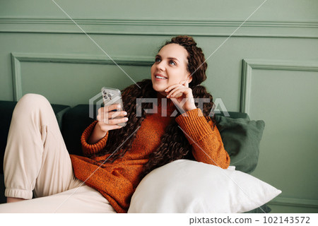 Happy Young Woman Using Cell Phone for E-Commerce Shopping and Entertainment at Home. Cheerful Woman 102143572