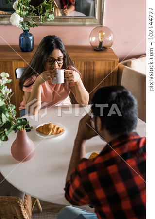 Young diverse loving couple eating croissant and talks together at home in breakfast time. Communication and relationship concept 102144722