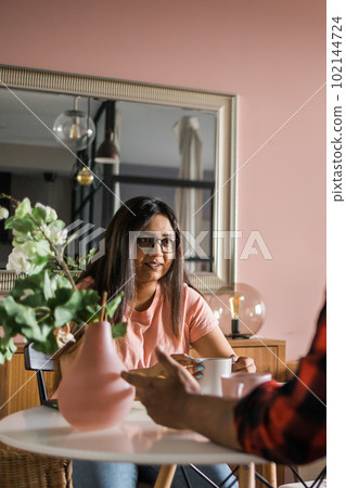 Happy couple eating breakfast and talking at dining table in morning. Indian girl and latino guy. Relationship and diversity concept Happy couple eating breakfast and talking at dining table in morning. Indian girl and latino guy. Relationship and diversity concept 102144724