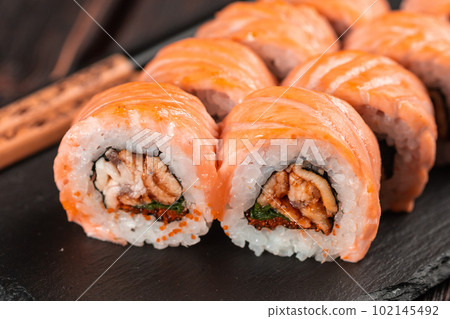 Sushi roll maguro with salmon, smoked eel, avocado and tobiko on black board close-up. Sushi menu. Japanese food. Sushi roll maguro with salmon, smoked eel, avocado and tobiko on black board close-up. Sushi menu. Japanese food. 102145492