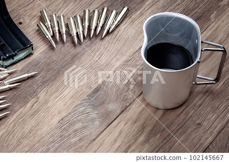 Cartridges and black coffee. Assault rifles cartridges and cup of coffee on wooden table Cartridges and black coffee. Assault rifles cartridges and cup of coffee on wooden table 102145667