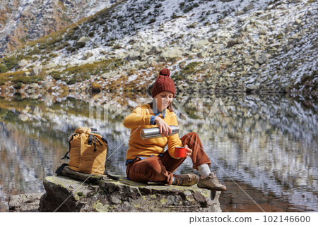 woman on mountain lake is resting and drinking tea, solo travel for one person. 102146600