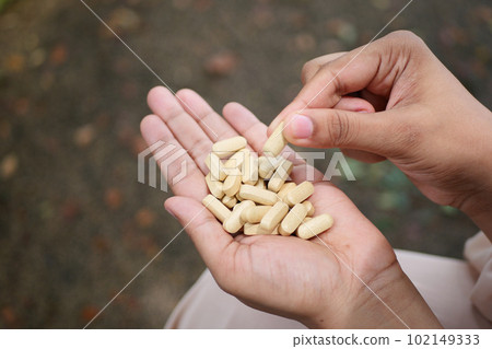 rear view of women hand taking medical tablet  102149333