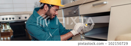 Focused professional worker in uniform is assembling furniture on kitchen. Repair concept 102150729