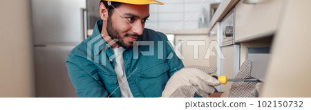 Smiling professional worker in uniform is assembling furniture on kitchen. Repair concept 102150732