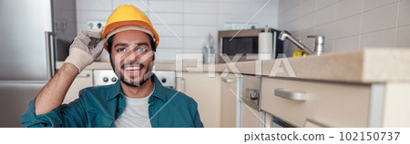 Smiling professional worker in uniform is assembling furniture on kitchen. Repair concept Smiling professional worker in uniform is assembling furniture on kitchen. Repair concept 102150737