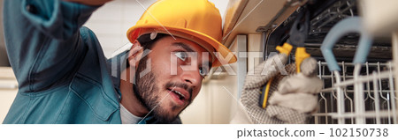 Close up of handyman in special clothing repairing dishwasher in modern kitchen 102150738