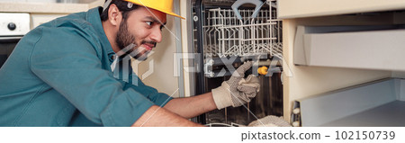 Focused handyman in special clothing repairing dishwasher in modern kitchen Focused handyman in special clothing repairing dishwasher in modern kitchen 102150739