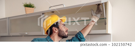 Focused professional worker in uniform is assembling furniture on kitchen. Repair concept Focused professional worker in uniform is assembling furniture on kitchen. Repair concept 102150742