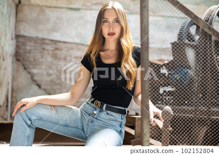 Woman in jeans and black tee shirt posing near steel mesh fencing in destroyed plant Woman in jeans and black tee shirt posing near steel mesh fencing in destroyed plant 102152804
