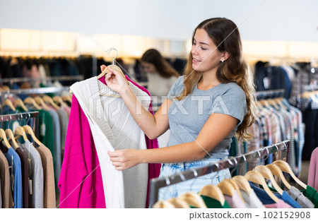 Dreamy young woman choosing season outfit clothes among the racks in a clothing store Dreamy young woman choosing season outfit clothes among the racks in a clothing store 102152908