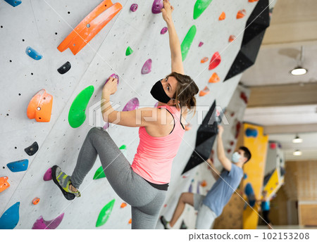 Woman in protective mask training at bouldering gym without special climbing equipment Woman in protective mask training at bouldering gym without special climbing equipment 102153208